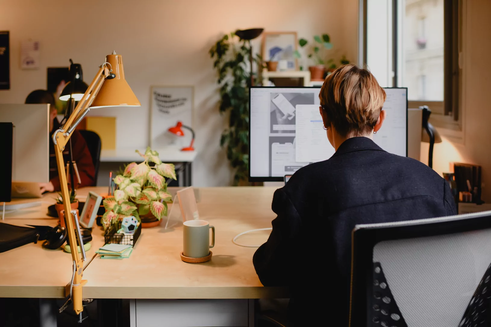 A member of the Médianes team works at their desk, with an orange architect's lamp in the foreground.