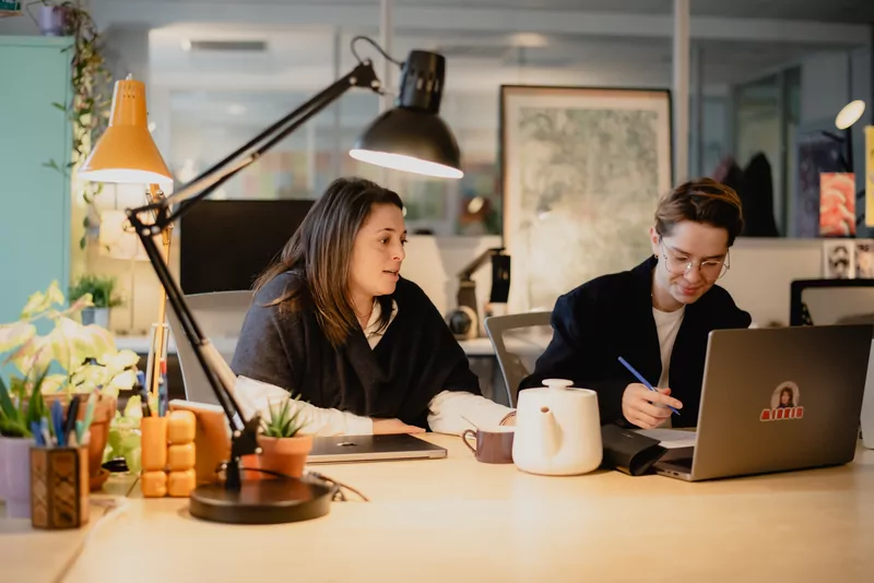 Two team members exchange ideas in front of a laptop.